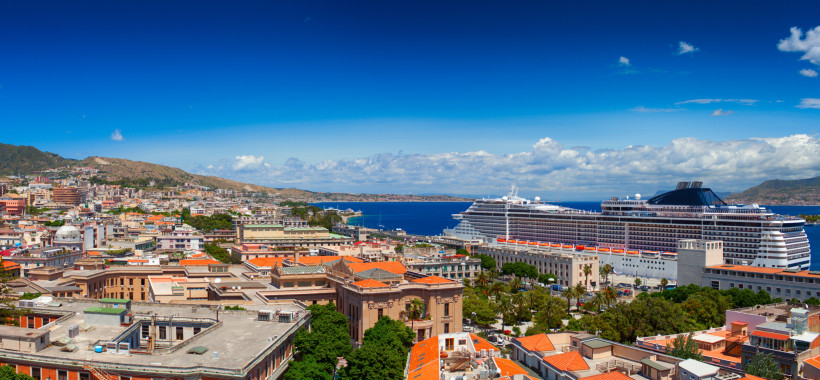 MSC Kreuzfahrtschiff im Hafen einer Küstenstadt MSC Kreuzfahrtschiff im Hafen vor einer Küstenstadt mit roten Dächern und blauem Himmel