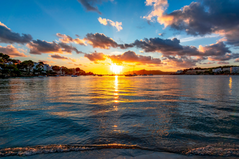 Sonnenuntergang über einer Bucht mit Segelbooten, Wolken und Küstenbebauung