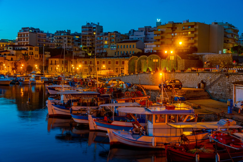 Hafen von Heraklion in der Abenddämmerung mit Fischerbooten, Stadtmauer und beleuchteten Gebäuden