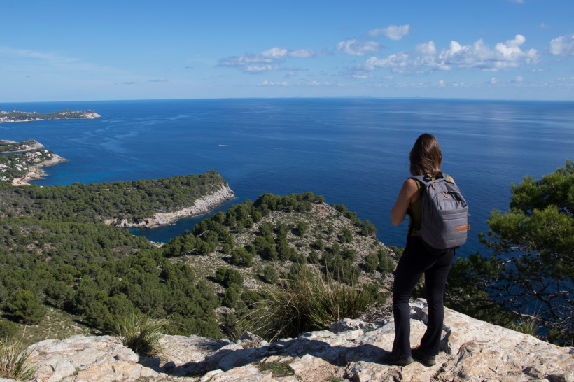 Wanderin mit Rucksack auf einem Felsvorsprung mit Blick über die Ostküste von Mallorca und das Meer