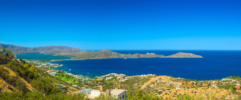 Blick auf die Bucht von Elounda mit Küstenort, blauem Meer und Inseln im Hintergrund