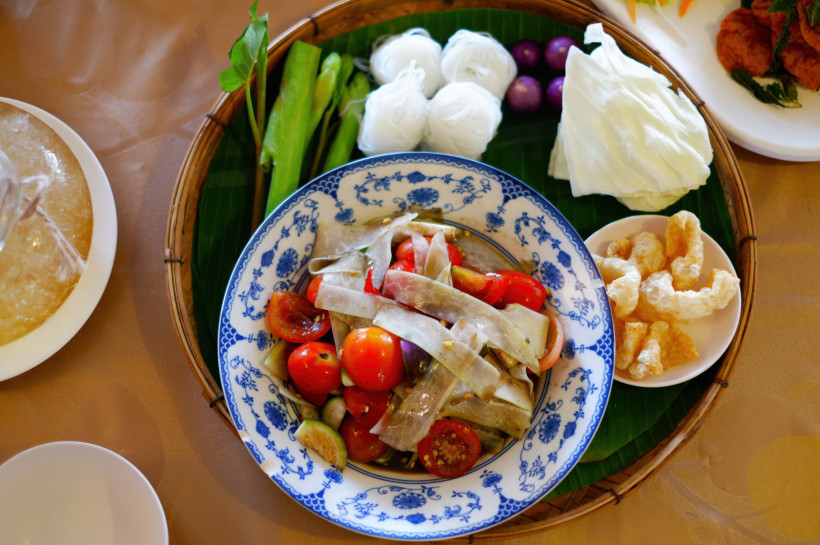 Thailand Pattaya Thailändisches Gericht mit Som Tam (Papayasalat), frischem Gemüse, Reispapier, Reisnudeln, kleinen Auberginen, Weißkohl und knusprigen Schweineschwarten, serviert auf einem runden Bambustablett mit Bananenblatt