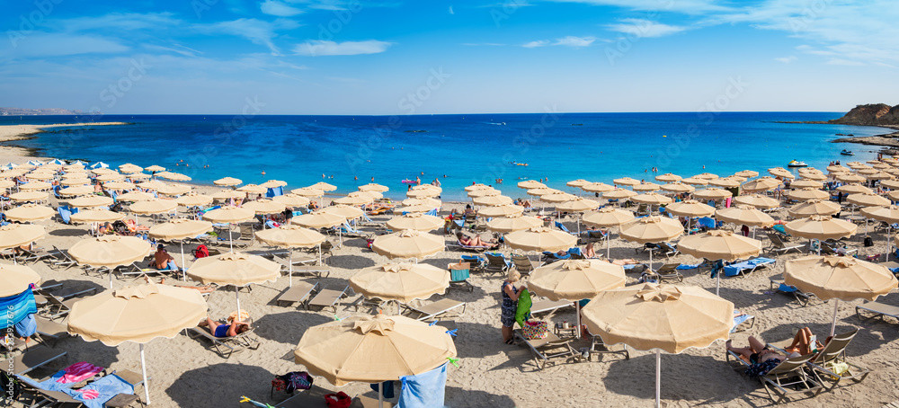 Großer Sandstrand auf Rhodos mit zahlreichen Sonnenschirmen, Badegästen und kristallklarem, türkisblauem Wasser.