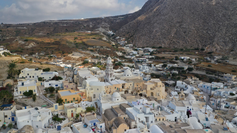 Santorini - Emporio Emporio auf Santorini aus der Luft: weiß gekalkte Häuser und markanter Glockenturm am Fuß des Profitis-Ilias-Berges, umgeben von kargen Hängen