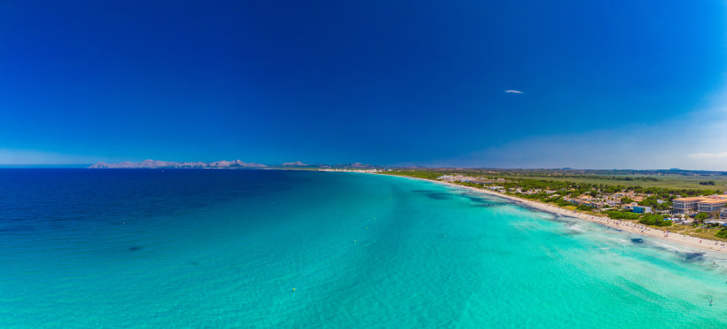 Luftaufnahme der Playa de Muro mit langem, breitem Sandstrand, türkisfarbenem Wasser und Übergang zur offenen Bucht von Alcudia