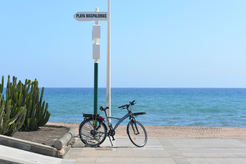 Fahrrad an der Strandpromenade vor dem Meer, Wegweiser „Playa Maspalomas“