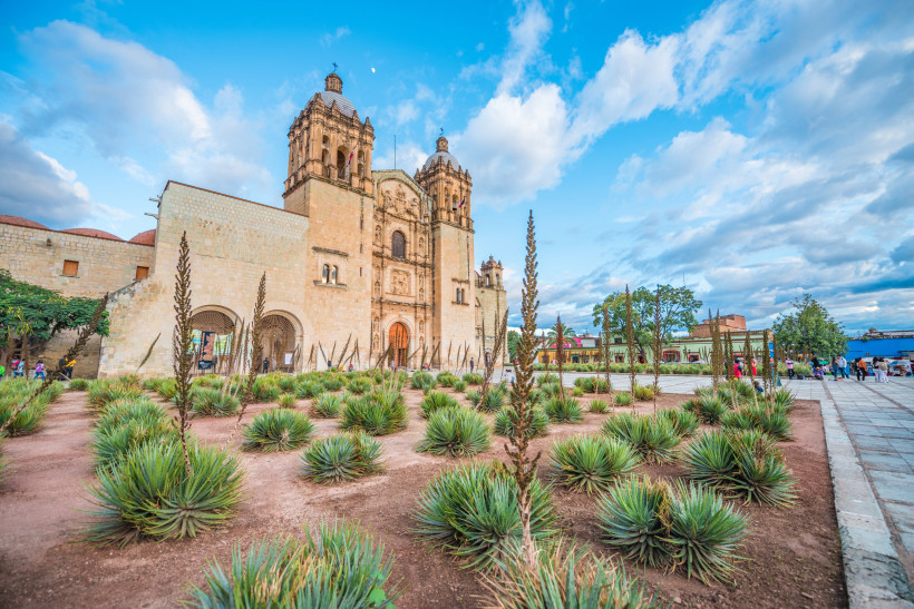 Dominikanische Republik - Santo Domingo Historische Kirche mit barocken Türmen; davor ein Garten mit Agaven und Kakteen unter blauem Himmel