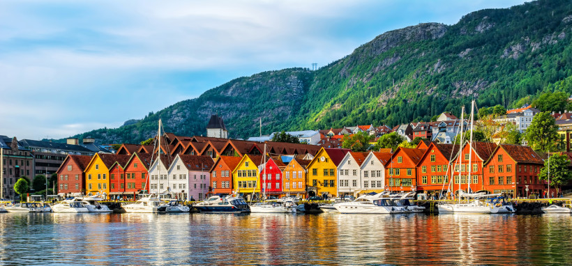 Bunte Holzhäuser am Hafen von Bergen mit Booten im Vordergrund und bewaldeten Bergen im Hintergrund
