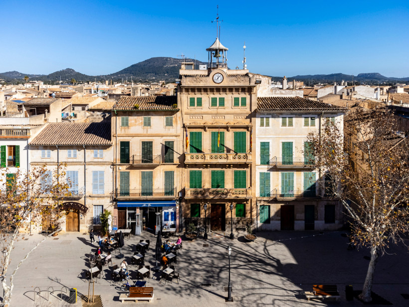 Historische Gebäude mit grünen Fensterläden an der Plaça d’Espanya, davor Cafétische und Stühle auf dem Platz