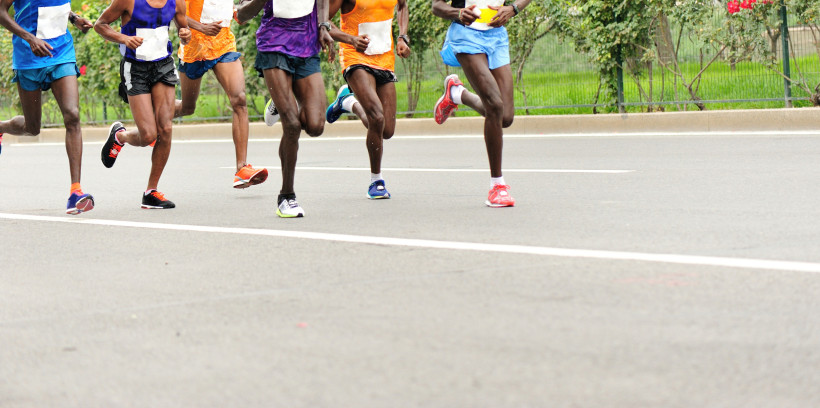 Gruppe von sechs Läufern in bunter Laufkleidung beim Marathon auf einer städtischen Straße. Nur Beine und Unterkörper sind im Bild, alle befinden sich im Laufschritt
