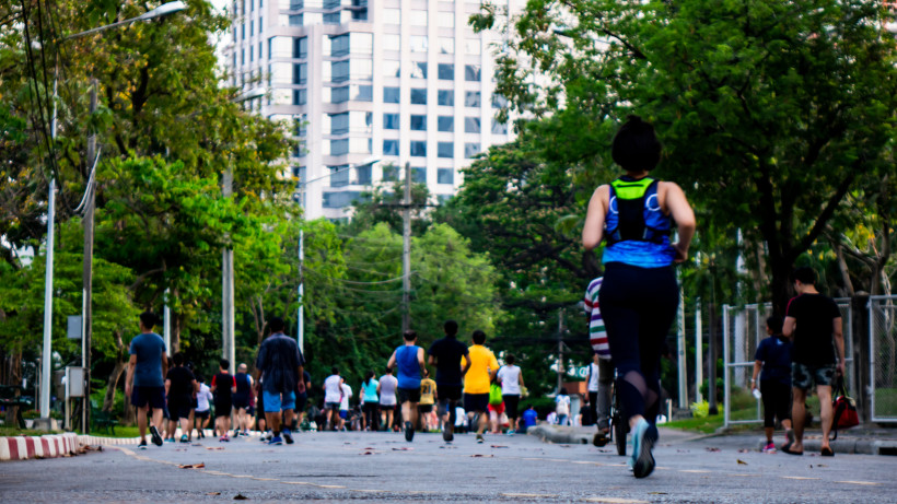 Thailand Menschen beim Joggen und Spazierengehen auf einer von Bäumen gesäumten Straße in einer Großstadt, im Hintergrund ein modernes Hochhaus.