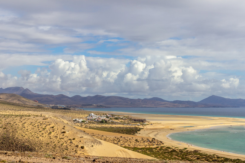 Küstenlandschaft am Risco del Paso mit Sanddünen, Lagune und Strand, dahinter Berge unter Wolkenhimmel