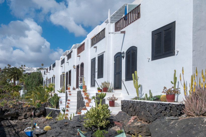 Traditionelle weiße Häuser in Puerto del Carmen – Lanzarotes Küstenarchitektur Weiße Häuser mit schwarzen Fensterläden, Kakteen und vulkanischen Steinen in Puerto del Carmen auf Lanzarote – traditionelle kanarische Architektur am Meer.
