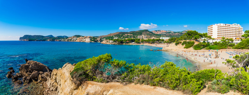 Blick über die Bucht von Playa Tora mit Sandstrand, türkisblauem Meer, Pinien und Hügeln im Hintergrund