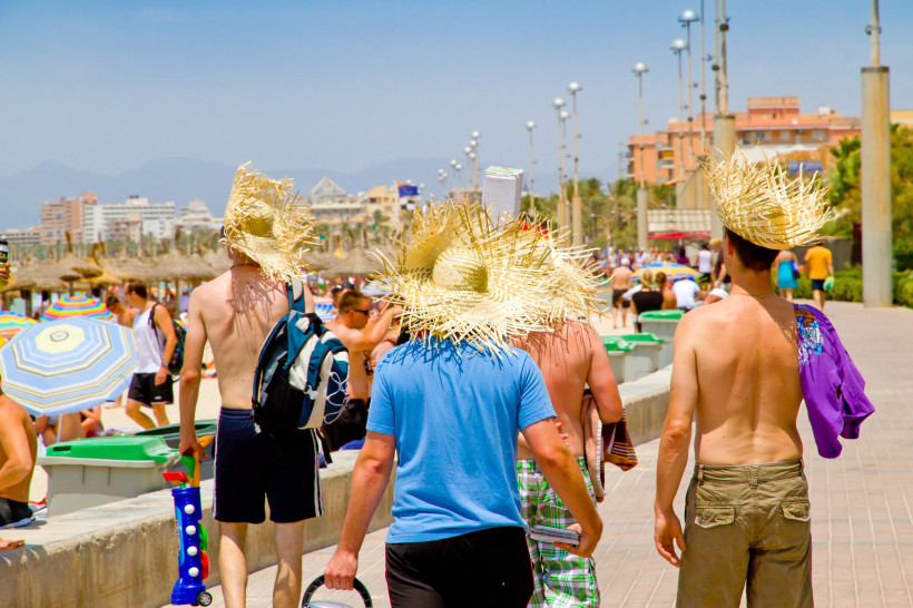 Menschen mit Strohhüten auf der Strandpromenade von El Arenal, im Hintergrund Strand und Hotels