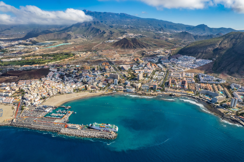 Atemberaubender Panoramablick auf Los Cristianos Panoramablick auf Los Cristianos auf Teneriffa mit Hafen, Sandstrand, türkisfarbenem Meer und umliegenden Bergen aus der Luftperspektive.