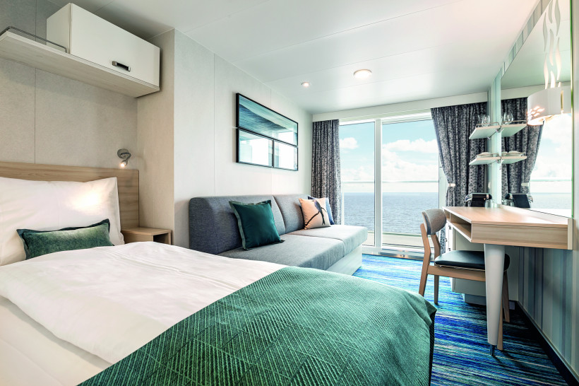 Innenansicht einer Balkonkabine auf Mein Schiff 1 mit Doppelbett, Sofa und Schreibtisch vor großer Balkontür mit Meerblick