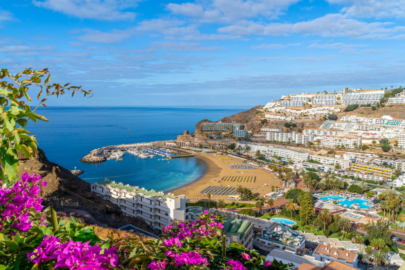 Puerto Rico de Gran Canaria – Panorama auf Strand und Yachthafen Panoramablick auf Puerto Rico de Gran Canaria mit Strand, Yachthafen, weißen Hotels am Hang und blühenden Bougainvilleen im Vordergrund
