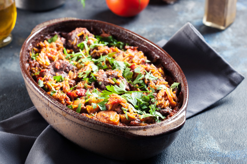 Giouvetsi in einer ovalen Auflaufform mit Kritharaki, Fleischstücken, Tomatensauce und Petersilie
