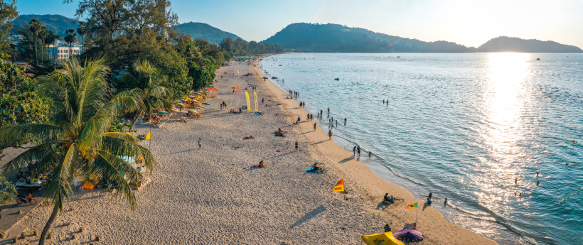 Tagesaufnahme vom Patong Beach auf Phuket mit feinem Sand, Palmen und badenden Urlaubern – beliebtester Strand auf Phuket 2025/2026