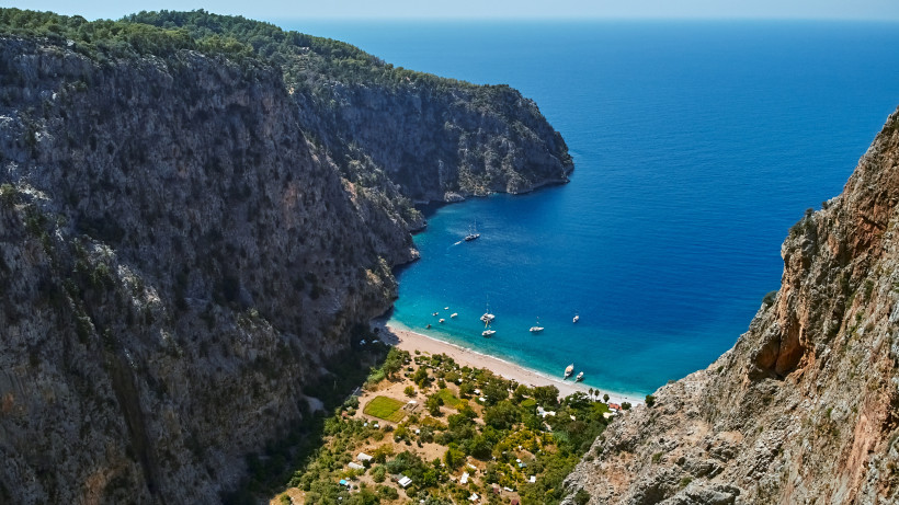 Blick auf Butterfly Bay in der Türkei mit Sandstrand, türkisblauem Wasser, Booten und steilen Felsklippen