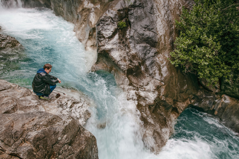 Ein Mann sitzt auf einem Felsen am rauschenden Wasserfall der Sapadere Schlucht bei Alanya – ein Naturerlebnis mit türkisblauem Wasser und beeindruckender Felslandschaft.
