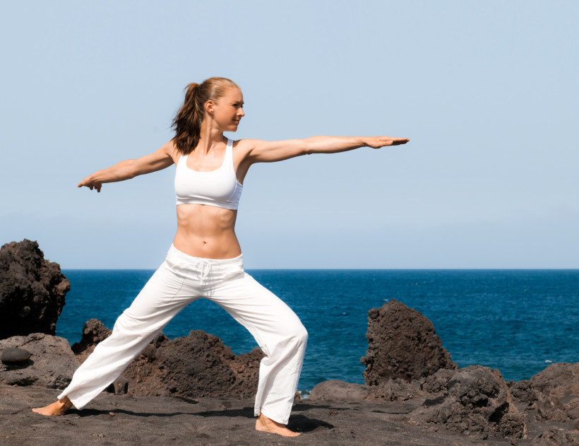 Yoga auf Lanzarote – Entspannung am Meer zwischen Lavafelsen Frau praktiziert Yoga am Strand von Lanzarote vor dem Meer und vulkanischen Felsen.