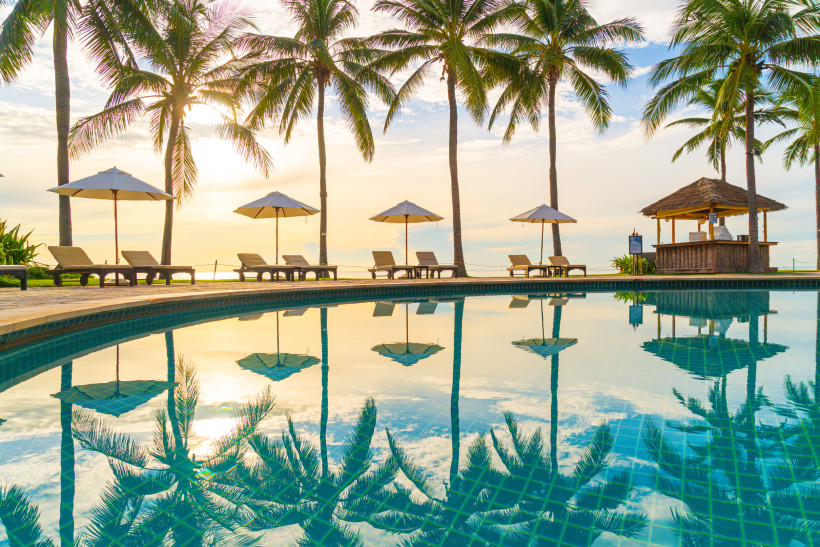 Luxusferien in Mexiko Luxuriöser Poolbereich mit Liegestühlen, Sonnenschirmen und Palmen, die sich im ruhigen Wasser spiegeln, bei Sonnenuntergang am Strand