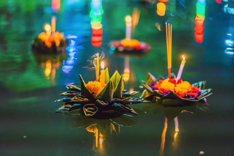 Thailand Pattaya Traditionelle schwimmende Krathong-Boote aus Bananenblättern mit Blüten, Kerzen und Räucherstäbchen treiben bei Nacht auf dem Wasser. Bunte Lichter spiegeln sich auf der Wasseroberfläche – festliche Stimmung zum Loi-Krathong-Fest in Thailand