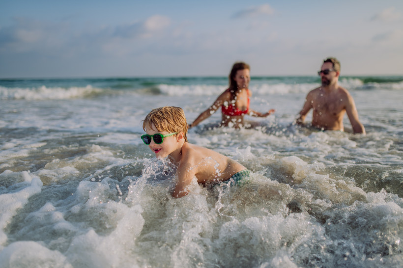Familie spielt im Meer bei Ierapetra; Kind mit Sonnenbrille in der Brandung, zwei Erwachsene im Hintergrund
