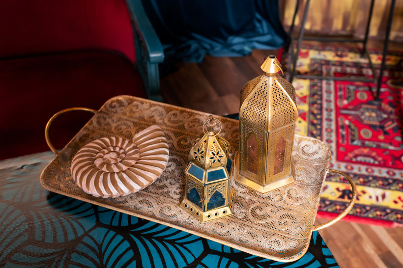 Ägypten - Sharm el Sheikh Ein kunstvoll verziertes goldenes Tablett mit zwei traditionellen orientalischen Laternen und einer dekorativen Muschel in Spiralenform steht auf einem bunt gemusterten Tisch. Im Hintergrund sind ein roter Teppich mit orientalischem Muster und ein Samtvor