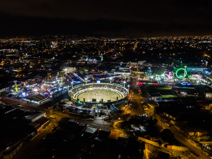Fiestas de Zapote, Costa Rica Luftaufnahme eines beleuchteten Festgeländes bei Nacht mit einer großen, runden Arena im Zentrum und zahlreichen bunten Fahrgeschäften drumherum.