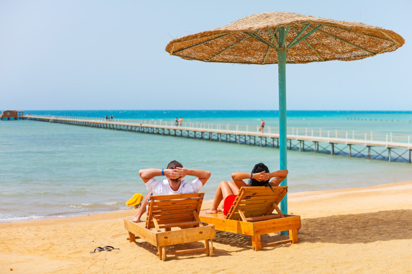 Paar entspannt auf Sonnenliegen unter einem Sonnenschirm am Strand mit Blick auf das türkisfarbene Meer