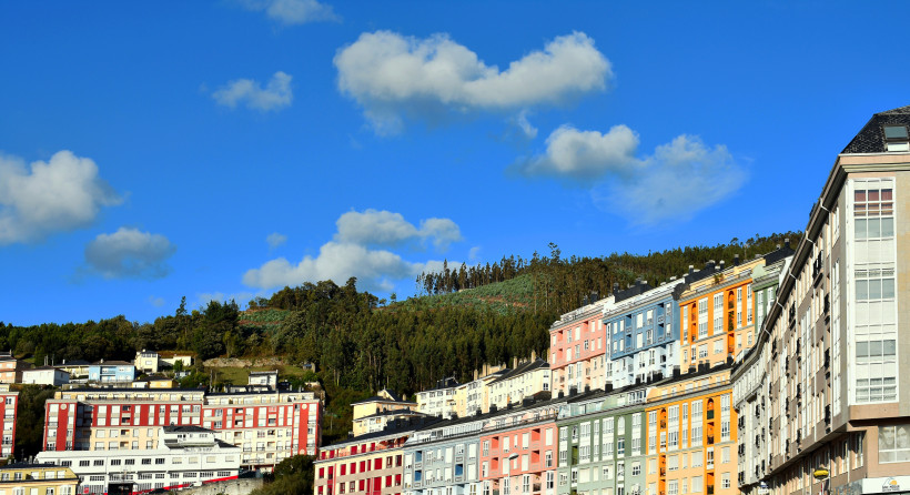 Bunte Wohnhäuser an einem Hang in Viveiro unter blauem Himmel mit Wolken
