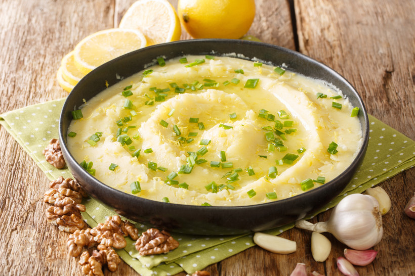 Schüssel mit Skordalia, mit Olivenöl und gehacktem Schnittlauch, daneben Zitronen, Knoblauch und Walnüsse