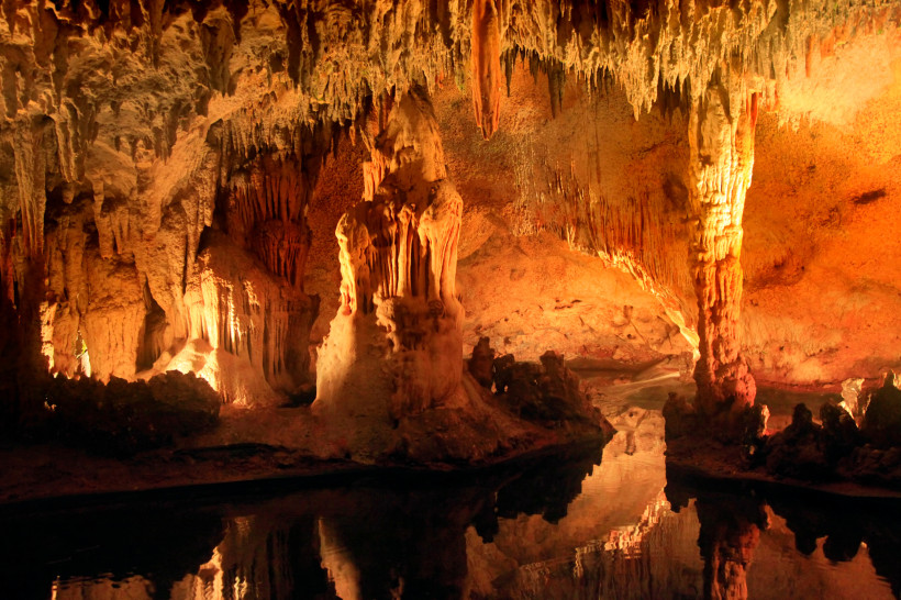 Dominikanische Republik Beeindruckende Tropfsteinhöhle mit spektakulären Stalaktiten und Stalagmiten in warmen Rottönen. Die Spiegelung der Felsformationen im Wasser verstärkt die mystische Stimmung.