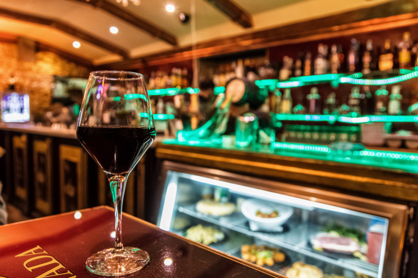 Mallorca Nahaufnahme eines Glases Rotwein auf einem Tisch in einer Bar mit beleuchteten Regalen und Theke im Hintergrund