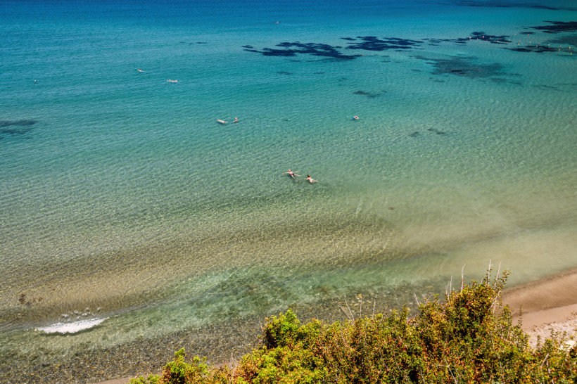 Ruhiger Strand bei Bali mit seichtem, klarem Wasser und zwei Schwimmenden. Ruhiger Strand bei Bali mit klarem, seichtem Wasser; zwei Personen schwimmen nahe der Küste.