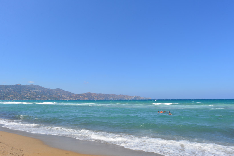 Blick auf den Amoudara Beach mit Sandstrand, türkisfarbenem Meer und Bergen im Hintergrund