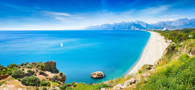 Panoramablick auf den Konyaalti Beach mit türkisfarbenem Meer, Küstenlinie und Gebirge im Hintergrund
