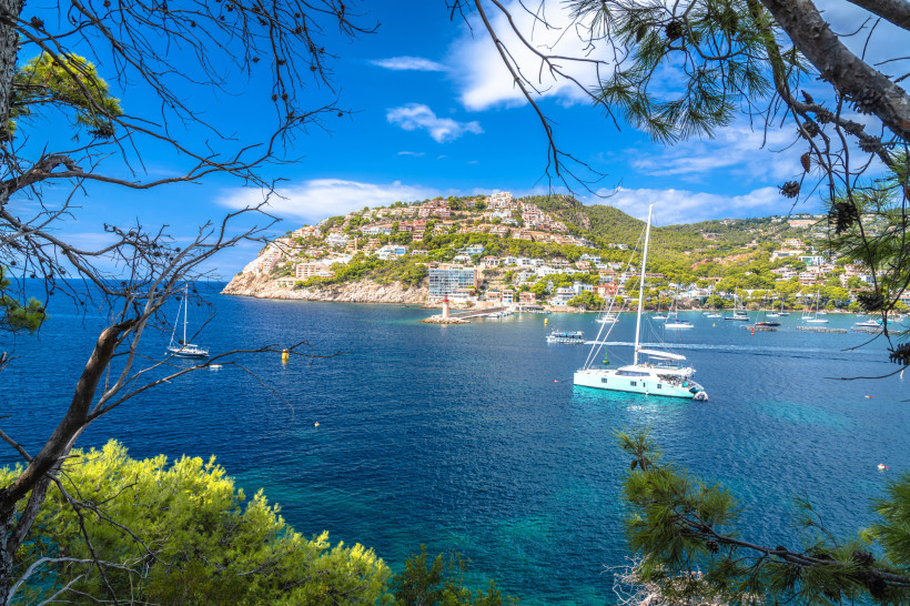 Blick auf die Bucht von Port d’Andratx mit Segelbooten und bebautem Hang unter blauem Himmel