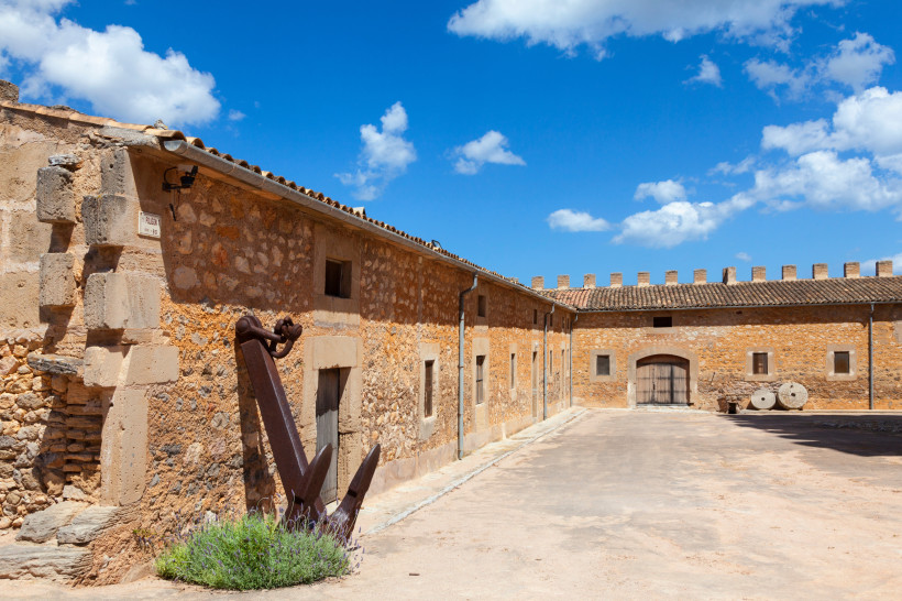 Innenhof der Torre de Canyamel mit Natursteinmauern, Zinnen und großem Anker im Vordergrund