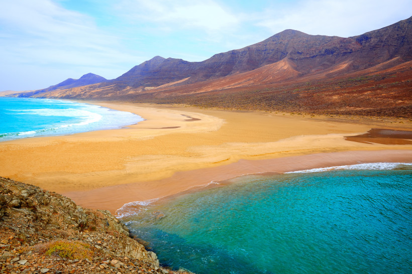 Blick auf den Strand von Cofete mit türkisfarbenem Meer und kargen Bergen im Hintergrund