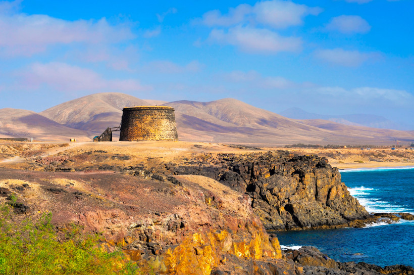 Castillo del Tostón auf einer felsigen Küste mit Blick auf den Atlantik und karge Berge im Hintergrund