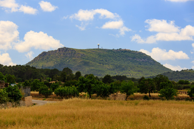 Blick auf den Puig de Randa mit bewaldetem Bergrücken und Radarkuppel unter blauem Himmel