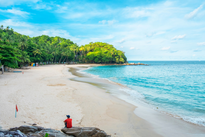 Einsamer Blick auf den idyllischen Freedom Beach in Phuket mit feinem weißen Sand, türkisblauem Meer und üppigem Dschungel im Hintergrund.