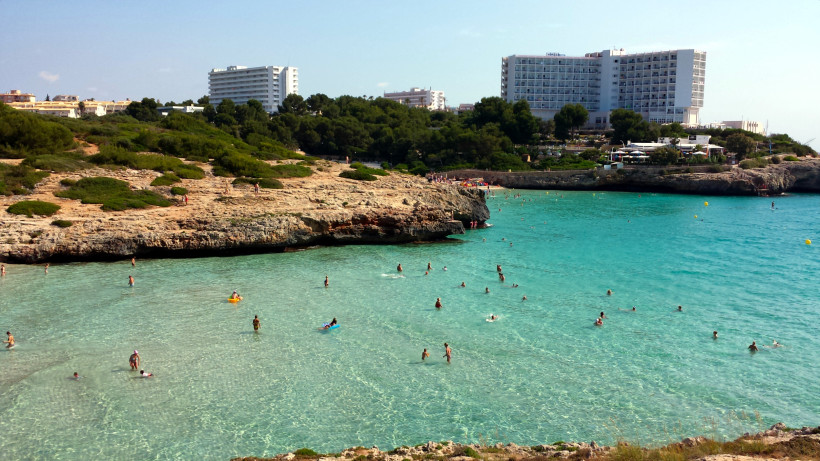 Sandbucht in Calas de Mallorca mit türkisfarbenem Wasser und mehrstöckigen Hotelanlagen oberhalb der Steilküste.