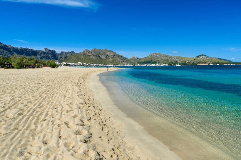 Sandstrand in Port de Pollença mit türkisfarbenem Wasser, Bucht und Bergen im Hintergrund