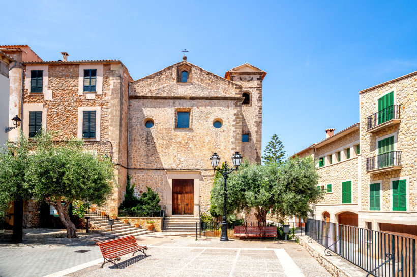 Banyalbufar, Mallorca Pfarrkirche Sant Joan Baptista im Dorf Deià auf Mallorca mit typischer Sandsteinfassade und kleinem Platz davor