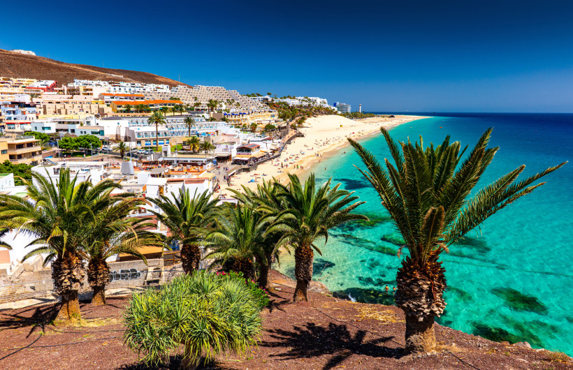 Morro Jable – Palmen, Hotels und der lange Sandstrand von Jandía Playa Aussicht über Morro Jable auf Fuerteventura mit Palmen, dem langen Strand von Jandía Playa, Hotels und dem Leuchtturm am türkisblauen Meer.